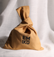 EMIKO SKINCARE 100% cotton Japanese knot bag, tan colour with the brand name 'EMIKO' printed in bold black letters, set against a draped white linen background.