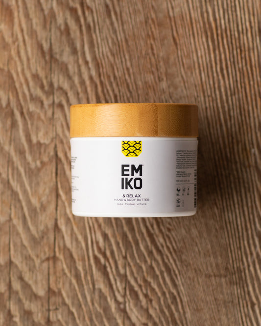 A white plastic jar  with bamboo lid of EMIKO & RELAX Hand & Body Butter placed on a rustic wooden surface.